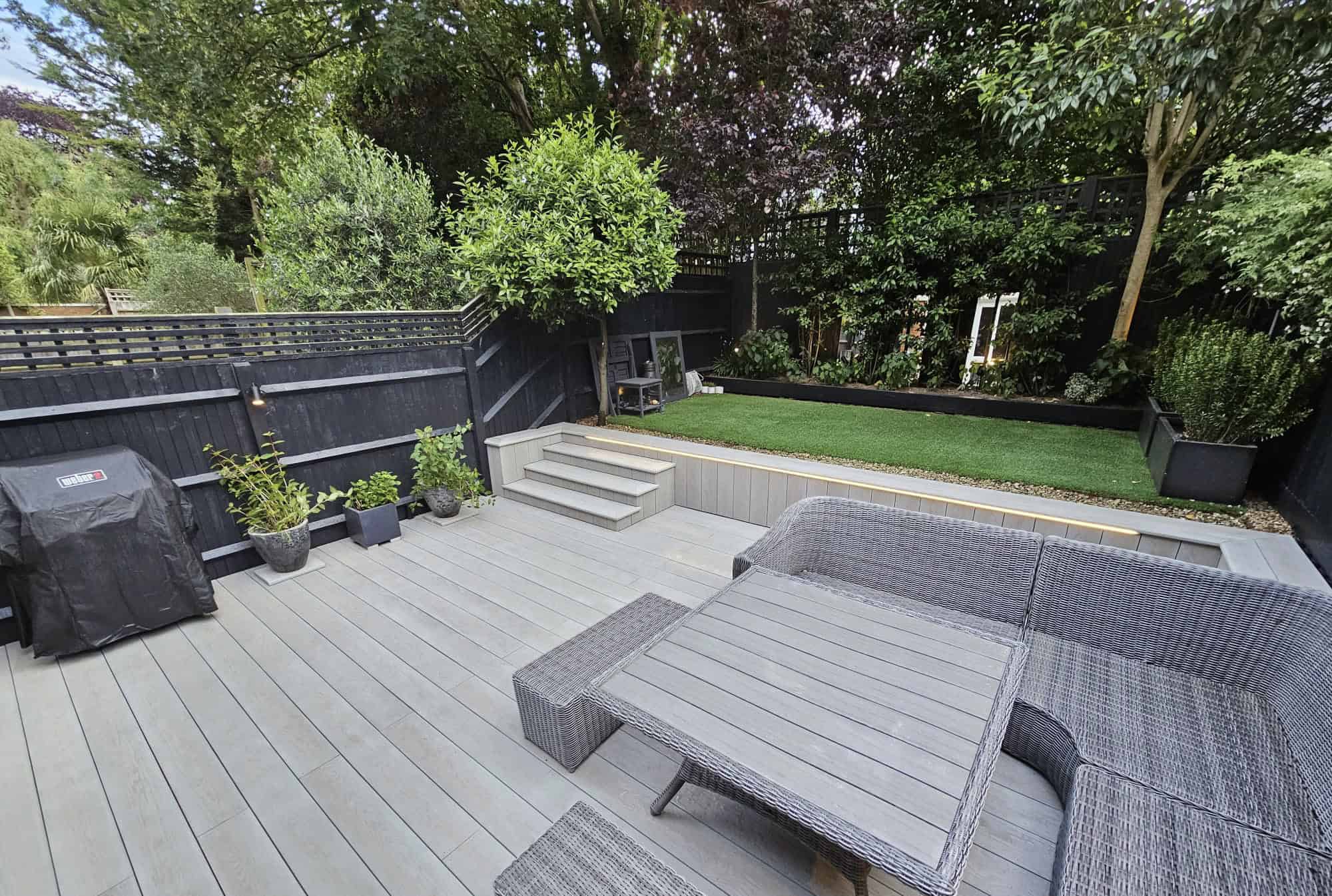 Modern composite decking in Windsor with outdoor seating and lush garden backdrop.